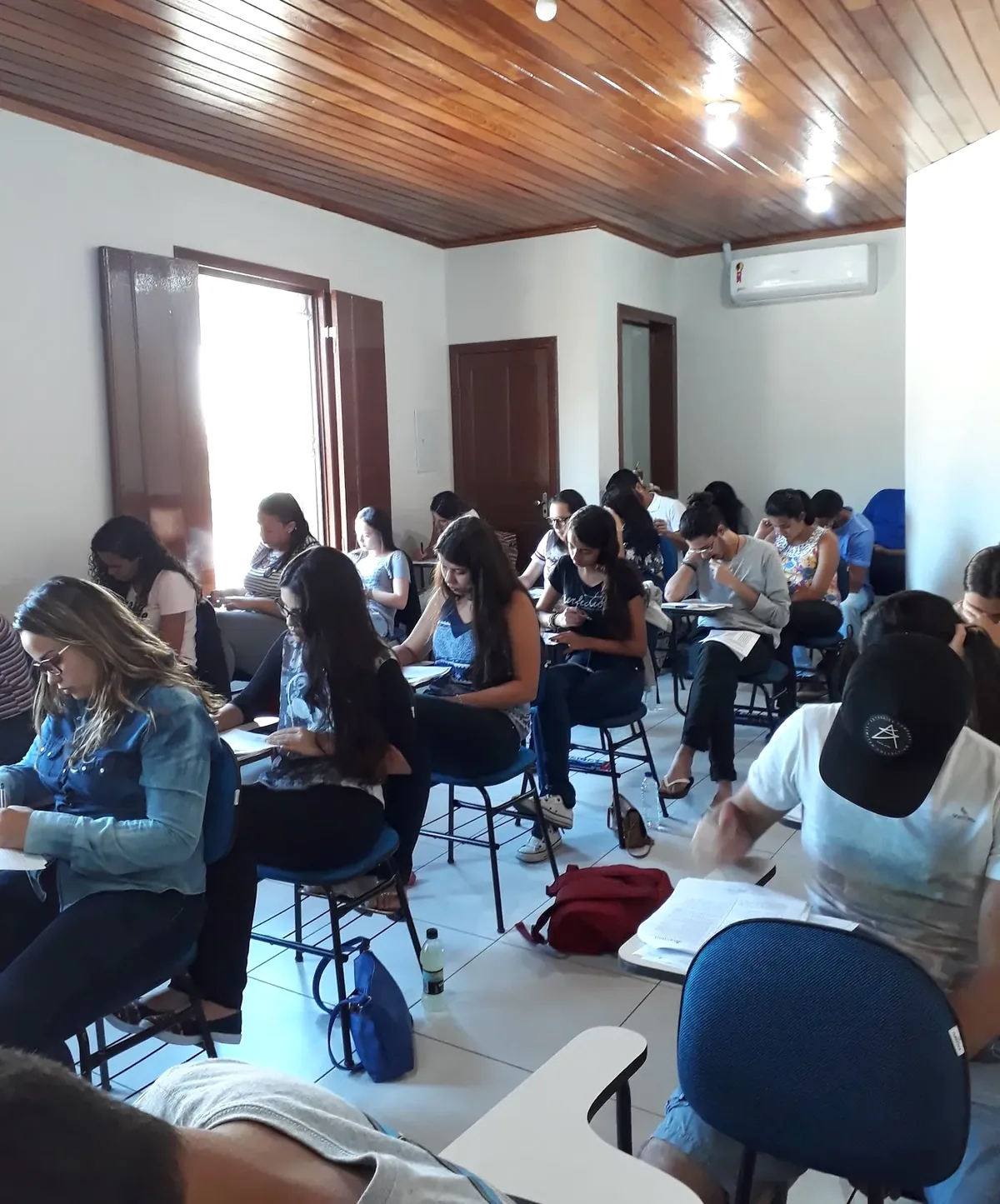 Sala do Merithus com alunos resolvendo questões nas carteiras, teto de madeira e janelas altas