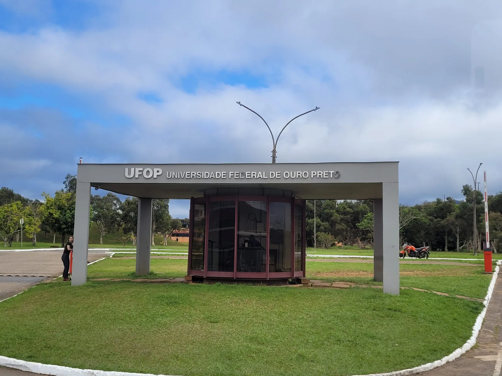 Portaria do campus da UFOP com o letreiro Universidade Federal de Ouro Preto, gramado e céu azul